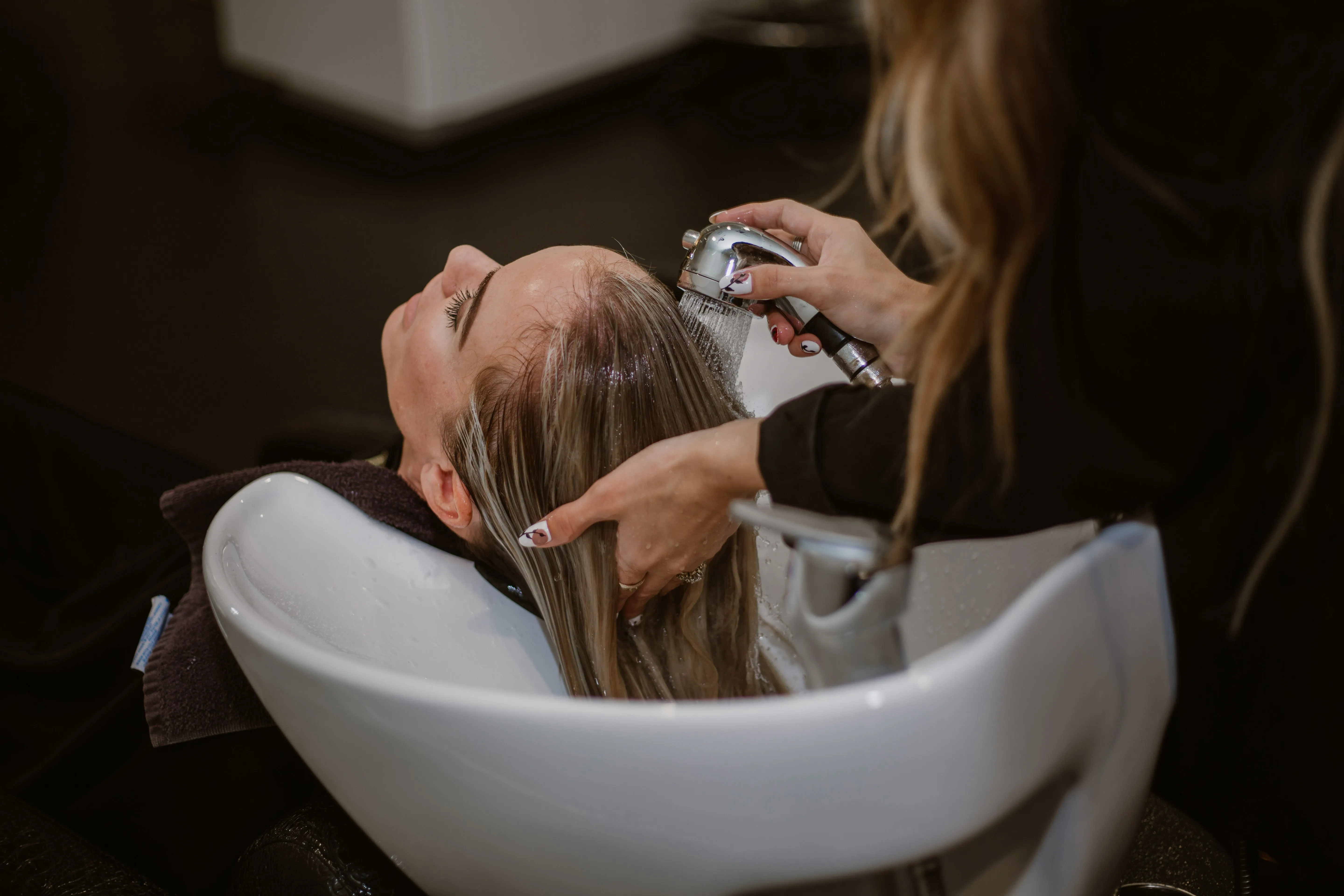 Stylist rinsing a client’s hair in a salon shampoo bowl